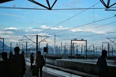 Silhouette people on electricity pylon against sky in city