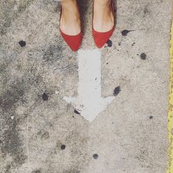 Low section of woman in red flat shoe standing in front of arrow sign on road