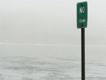 Information sign by sea against sky