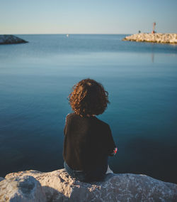 Woman sitting on rock over sea against sky