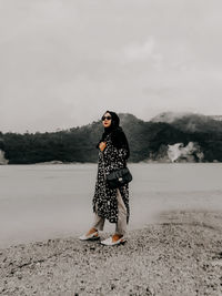 Rear view of woman standing on sand at lake against sky