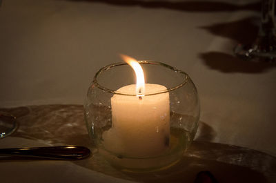 Close-up of illuminated candle in drinking glass on table