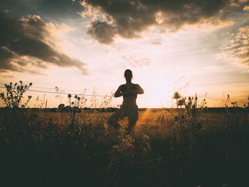 Woman meditating on field against cloudy sky during sunset