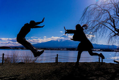 Silhouette man jumping on field against sky during winter