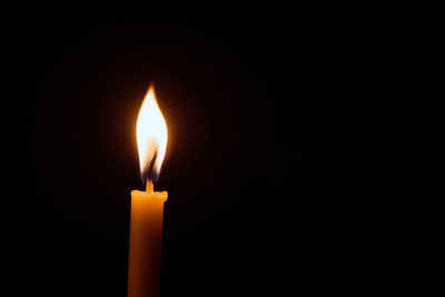 White candle flame closes upon a black background, candle burning in the dark with lights glow