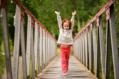 Portrait of girl with arms raised while standing on footbridge