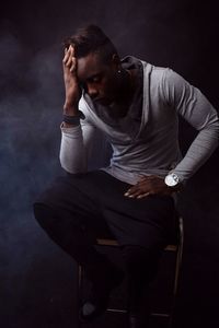 Young man sitting against black background