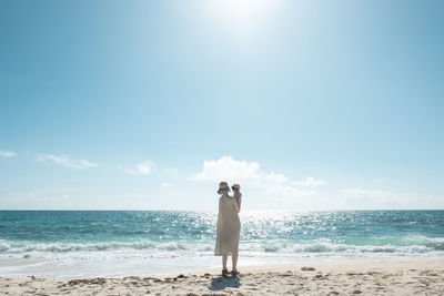 Full length of woman holding baby while standing on beach against sky