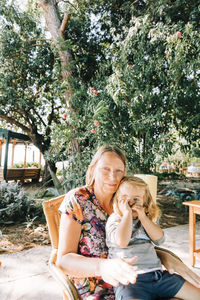 Mother and girl smiling while sitting on tree against plants