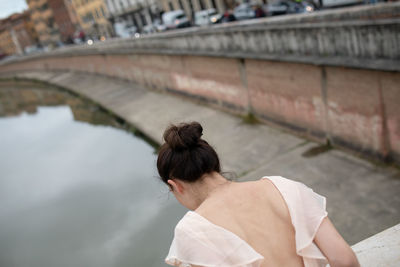 Rear view of woman leaning over wall in city