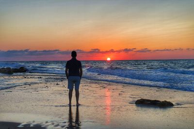 Rear view of man standing on beach during sunset