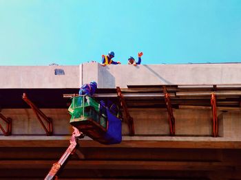 Low angle view of men working against clear sky