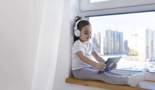 Young woman using laptop while sitting on window