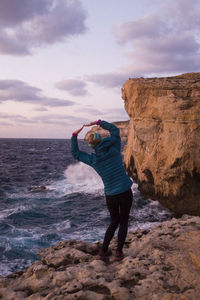 Rear view of woman standing at beach against sky during sunset