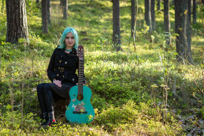 Hipster young woman with turquoise guitar sitting in forest