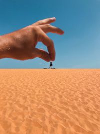 Optical illusion of hand holding woman on sand dune against clear sky