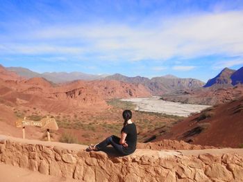 Full length of woman sitting on retaining wall at desert