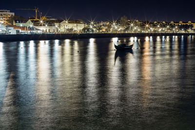 Boat sailing on river against illuminated city at night
