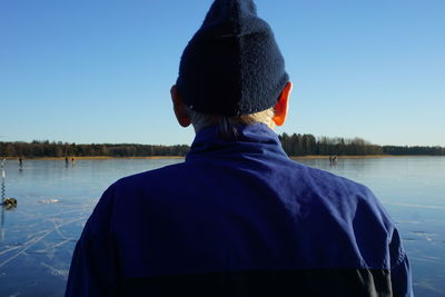 Rear view of senior man standing by lake against clear blue sky