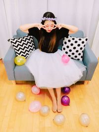 High angle view of woman gesturing while sitting on sofa amidst balloons at home