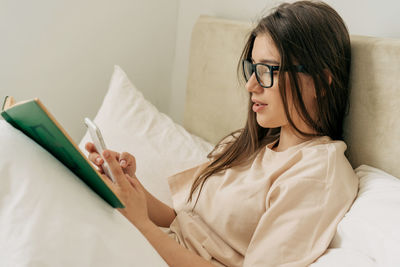 Young woman using mobile phone while lying on bed at home