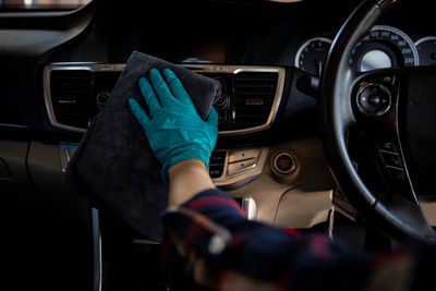 Worker women wear green gloves cleaning car interior console and air vent with gray microfiber cloth