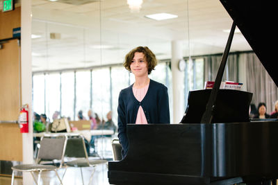 Teen girl smiles and stands by a grand piano after her recital