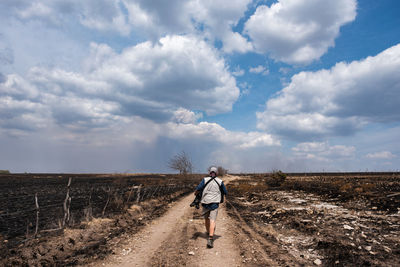 Rear view of man walking on field against sky