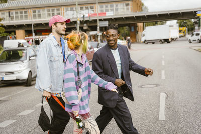 Happy non-binary person walking with gay friend on road in city