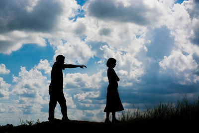 Silhouette couple on field against cloudy sky