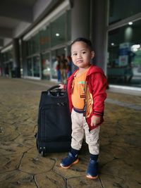 Portrait of smiling boy with luggage standing on floor