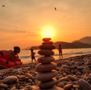 People on rocks at beach against sky during sunset