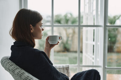 Close-up of woman holding coffee cup by window