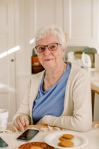 Portrait of retired senior woman sitting with smart phone at table in nursing home