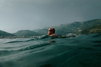 Man swimming in sea against mountains