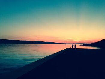 Silhouette people standing on sea against sky during sunset