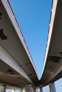 Low angle view of bridge against buildings against clear blue sky