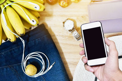 Cropped hand holding smart phone by fruits and personal accessories on table