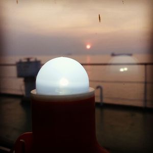 Close-up of illuminated lamp on table against sky at sunset