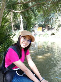 Portrait of smiling young woman wearing hat against trees