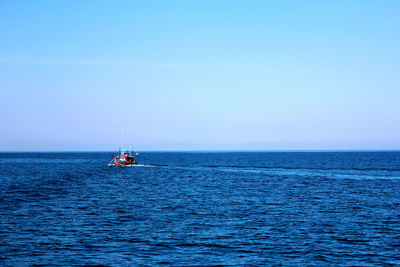 Boat sailing in sea against clear blue sky