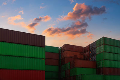 Low angle view of cargo containers at harbor against sky during sunset