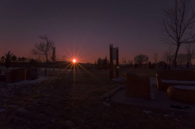 Bare trees on landscape at sunset