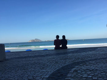 People on beach against clear blue sky