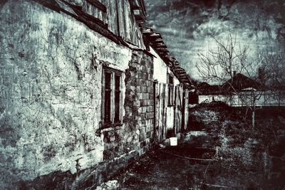 Abandoned house by bare trees against sky