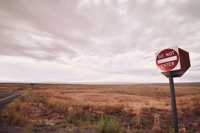 Road sign on field against sky