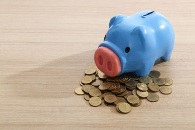 Close-up of blue piggy bank with coins on wooden table