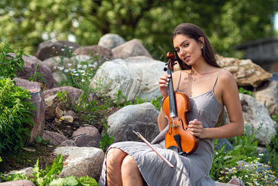 Beautiful brunette in a linen dress with a violin on a pile of boulders at an old country house