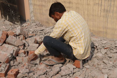 Side view of young man sitting against wall