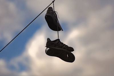 Low angle view of shoes hanging on cable against sky